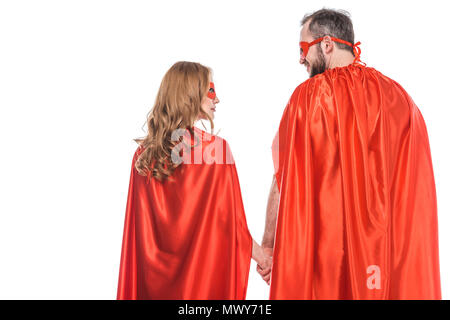 back view of super couple in masks and cloaks holding hands and looking at each other isolated on white Stock Photo