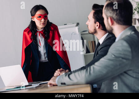 super businesswoman in mask and cape helping businessmen in office Stock Photo