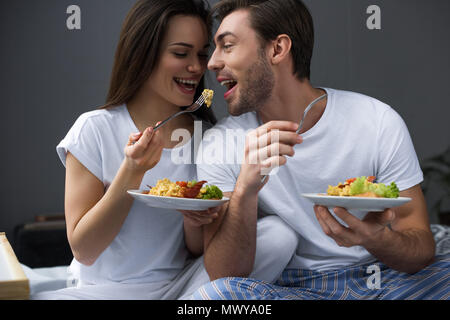 Attractive couple eating scrambled eggs in bed Stock Photo