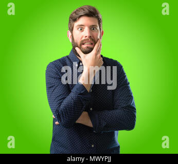 Young hipster man with big beard scared in shock, expressing panic and fear over green background Stock Photo