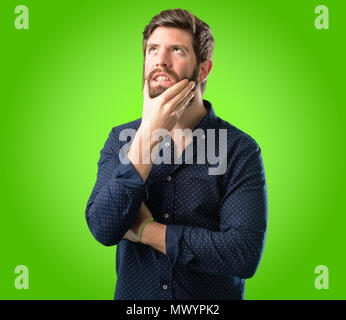 Young hipster man with big beard scared in shock, expressing panic and fear over green background Stock Photo