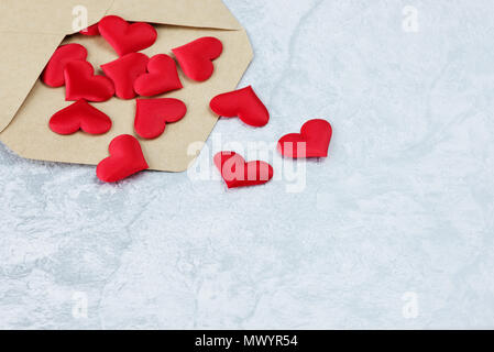 Several red silk hearts flying out of an open postal envelope made of kraft paper on a gray stone background, with copy-space Stock Photo