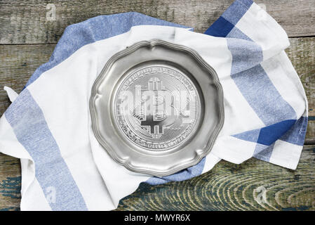 Empty pewter plate with bitcoin simbol and checkered kitchen towel on a rough wooden table, top view Stock Photo