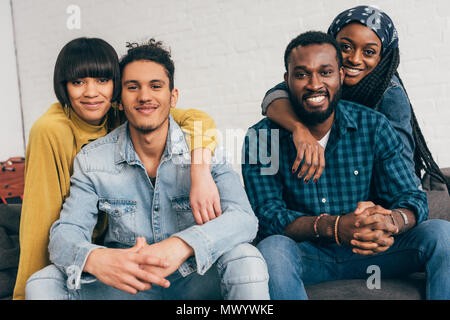 two young smiling couples sitting on couch and looking at camera Stock Photo