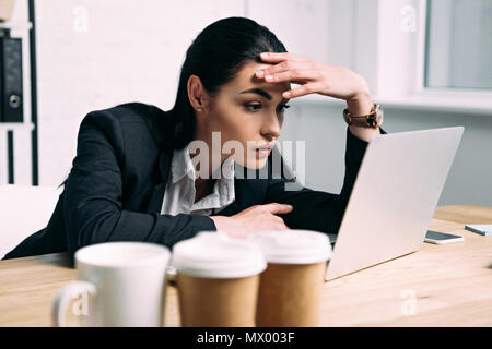 side view of tired businesswoman in suit working on laptop at workplace in office Stock Photo