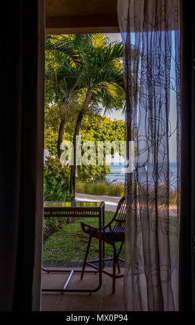 View of a tropical seaside beach through an open door with a lace curtain image with copy space in portrait format Stock Photo