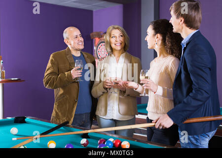 happy mature and young couples hanging out in billiard club together Stock Photo