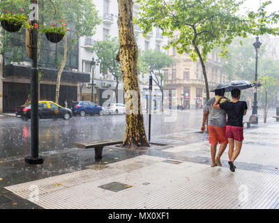 People walking with umbrellas in heavy rain storm on Avenida de Mayo in city centre Microcentro, Monserrat district in capital Buenos Aires, Argentina Stock Photo