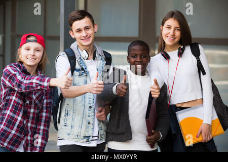 Happy four teenagers with folders and backpacks near college Stock Photo