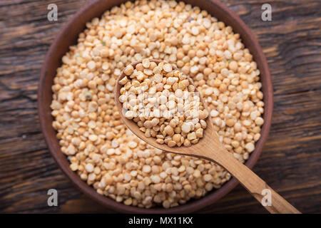 uncooked dried peas in an earthenware dish on a wooden surface, in the plate is a wooden spoon Stock Photo