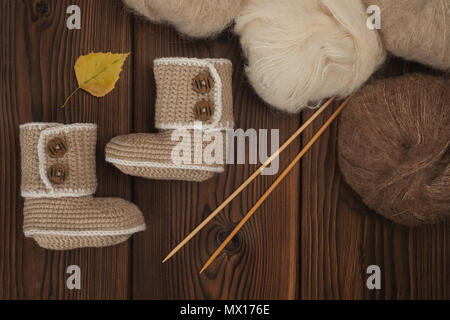 baby booties knitted by hand on a wooden background and skeins of wool Stock Photo