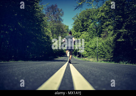 Rearview of a fit young man in sportswear running alone down the middle of a road in the country Stock Photo