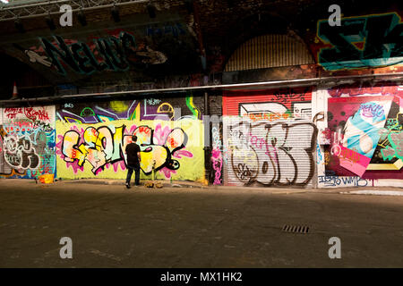 London, United Kingdom, April 17, 2018: A man is working on his graffiti in a dark underground alee in a centre of London, Waterloo. Stock Photo