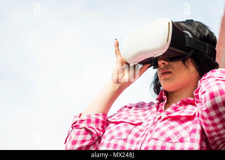 A young woman is wearing VR glasses. The girl spends her time in the open air using google virtual reality. Stock Photo