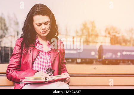 A woman is reading a book. A young and attractive girl learns to take exams at the university. Female relaxes reading interesting knowledge. The conce Stock Photo