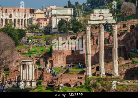 Visiting Roman Forum. Tourists walking among ancient ruins with Coliseum in the background Stock Photo