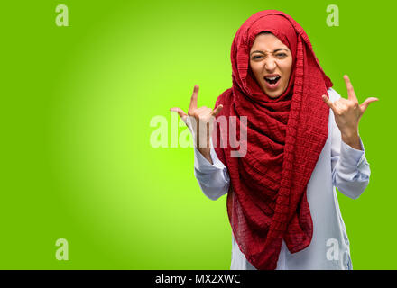 Young arab woman wearing hijab making rock symbol with hands, shouting and celebrating Stock Photo