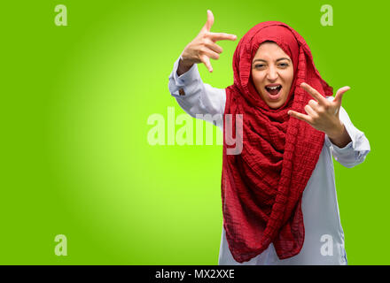 Young arab woman wearing hijab making rock symbol with hands, shouting and celebrating Stock Photo