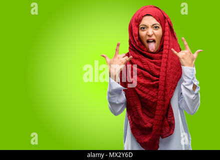 Young arab woman wearing hijab making rock symbol with hands, shouting and celebrating with tongue out Stock Photo