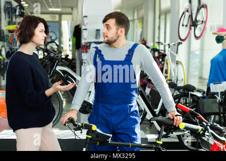 Young cheerful  man seller demonstrating bicycle to woman client in store Stock Photo