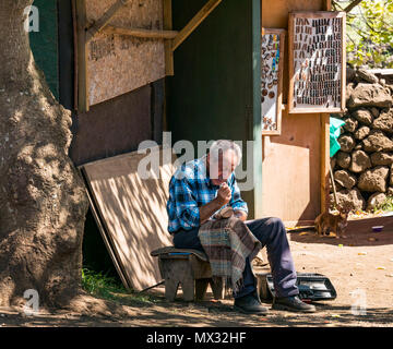 Old man hand sitting on stool in shade carving wooden Moai figure for sale to tourists, Rano Raraku quarry, Easter Island, Rapa Nui, Chile Stock Photo