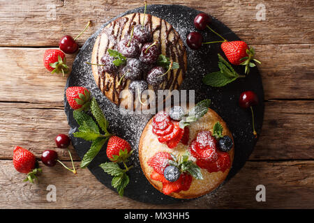 Biscuit cakes are decorated with chocolate, powdered sugar, mint, and summer berries close-up on a slate board. horizontal top view from above Stock Photo
