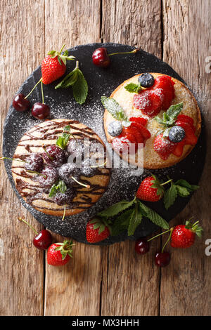 Biscuit cakes are decorated with chocolate, powdered sugar, mint, and summer berries close-up on a slate board. Vertical top view from above Stock Photo