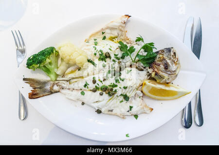 Fine dining: a main course of grilled sea bream (dorade) served on a white plate with a garnish of capers, broccoli and cauliflower and slice of lemon Stock Photo