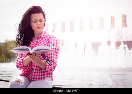 A woman is reading a book. A young and attractive girl learns to take exams at the university. Female relaxes reading interesting knowledge. Stock Photo