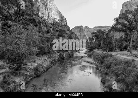 Overlooking a river with trail on one side and steep rock mountains on the other under clear sky. Stock Photo