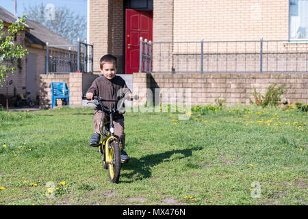 a boy rides his bike on a hot summer day. Boy riding a bicycle in the yard on a background of a brick house. Stock Photo