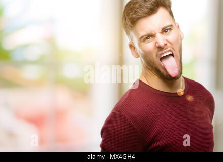 Handsome young man sticking out tongue at camera at sign of disobedience, protest and disrespect Stock Photo