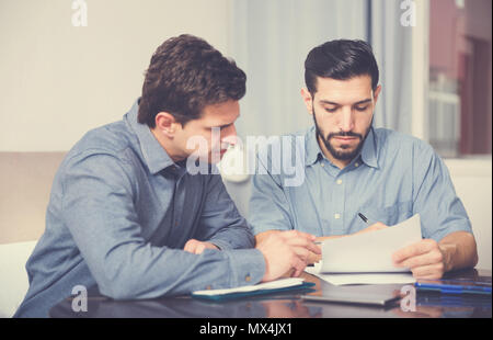 Two young men in serious discussion at home table while analysing documents together Stock Photo