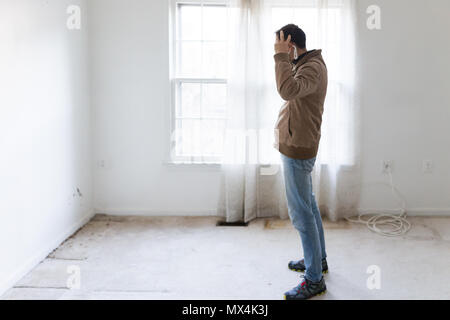 Young man in mask standing looking at room wall carpet floor flooring, white painted walls, during remodeling renovation, cleaning, inspection of dirt Stock Photo
