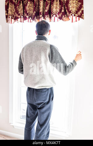 Man standing in front of bright window in home room adjusting old-fashioned retro blinds curtains Stock Photo