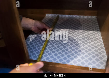 Man hands placing protective adhesive liner sheet, yellow measuring tape inside on wooden cabinets in kitchen drawers Stock Photo