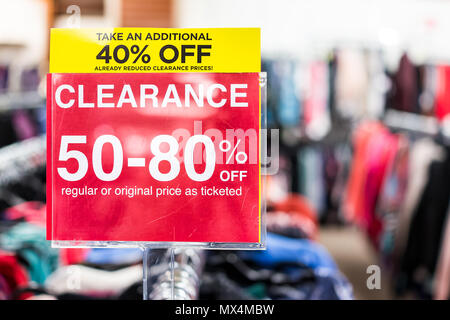 Many clothes bokeh in discount store, garments hanging on racks hangers row closeup with large red clearance sign, reduced prices Stock Photo