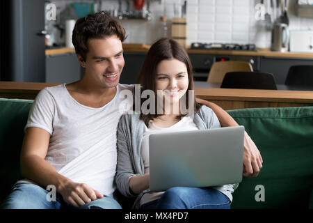 Smiling millennial couple using laptop computer sitting on kitch Stock Photo