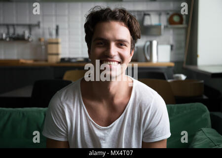 Smiling man looking at camera sitting on kitchen sofa, portrait Stock Photo