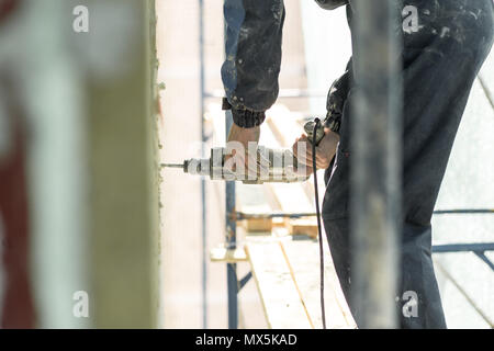 Hand drilling on the scaffolding on altitude. Concept repairing the wall panel. Stock Photo