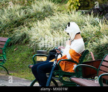 Unidentifiable asian man sitting on a bench wearing a kawaii panda hat in Taipei Taiwan : panda mania concept Stock Photo