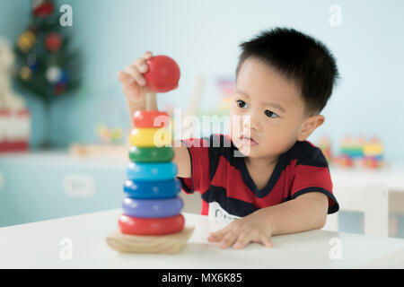 Adorable Asian Toddler baby boy sitting on chair and playing with color developmental toys at home. Stock Photo