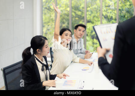 Asian woman is raising her hands has question while businessman presentation about business sale report at the meeting room Stock Photo