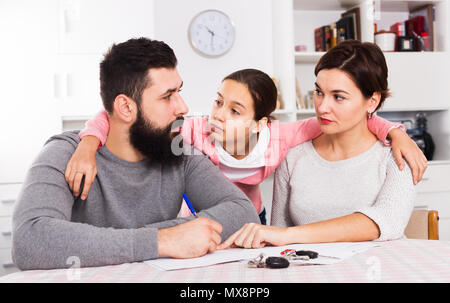 Young sad parents signing papers for divorce while their daughter at home Stock Photo