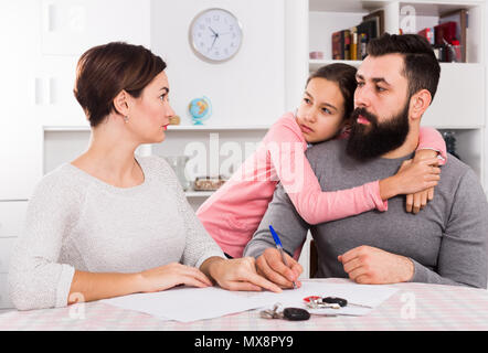 Young parents signing papers for divorce while their daughter at home Stock Photo