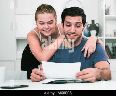 Happy young man and woman reading mail together and checking accountancy in home interior Stock Photo
