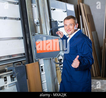 friendly smiling man in workwear cutting plywood using electric saw machinery Stock Photo