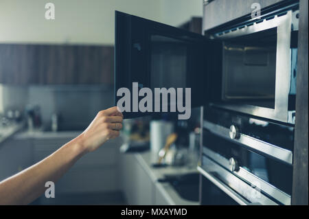 A young woman is opening the microwave in her modern apartment Stock Photo