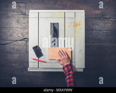 The hand of a young man operating a tablesaw, theere is a pencil and smartphone on the saw Stock Photo