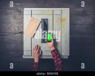 A young man operating a tablesaw is holding a chroma key smart phone Stock Photo
